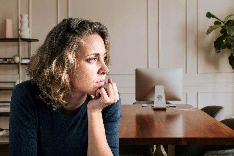 Symbolbild einer Frau in Gedanken, die den Blick senkt - Ausdruck von innerer Zerrissenheit, emotionaler Erschöpfung und Identitätssuche
