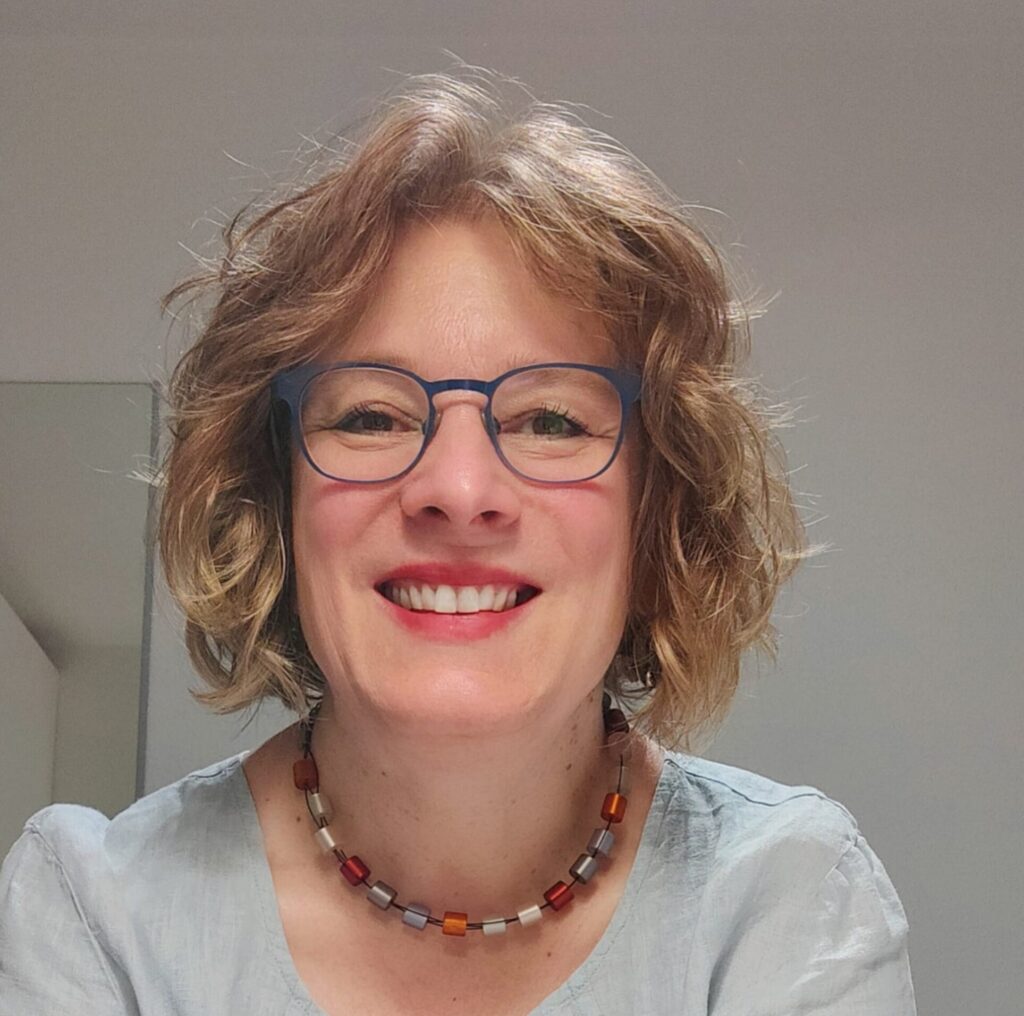 Portraitfoto von Corinna von der Mühlen, lächelnd, vor hellem Hintergrund